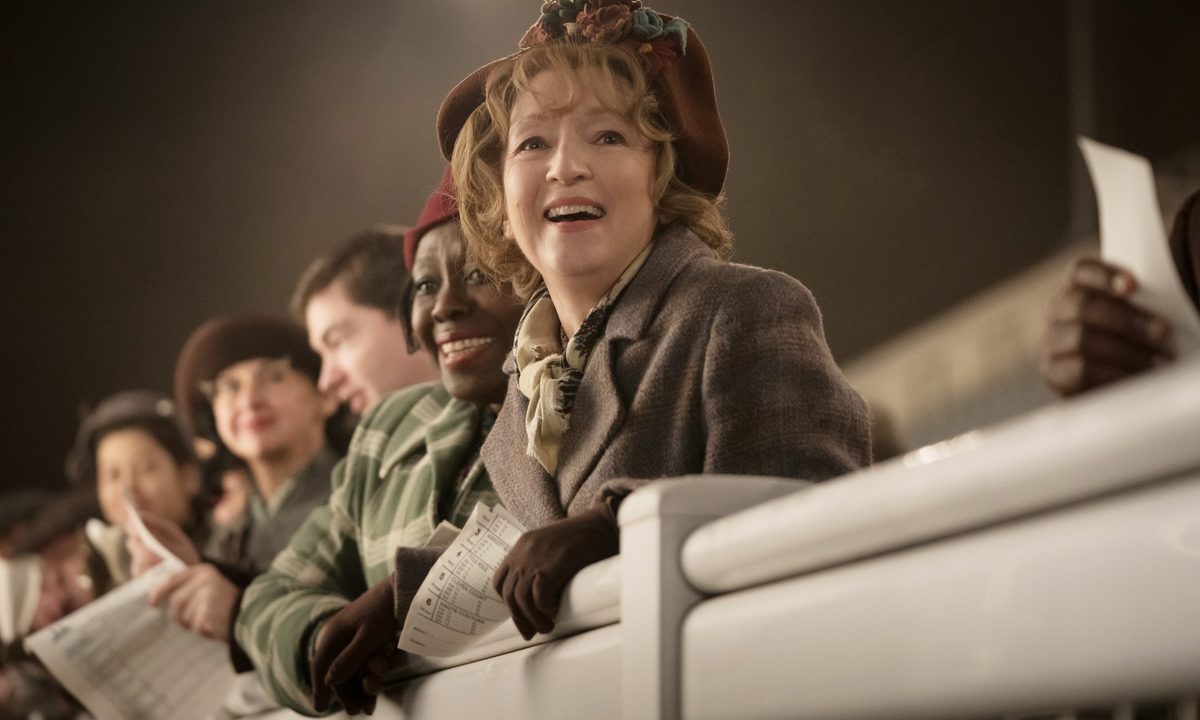 People look on at a racetrack in Mrs. Harris Goes to Paris.
