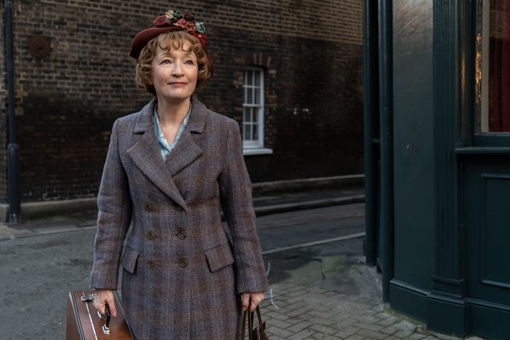 A woman stands at a street corner in Mrs. Harris Goes to Paris.
