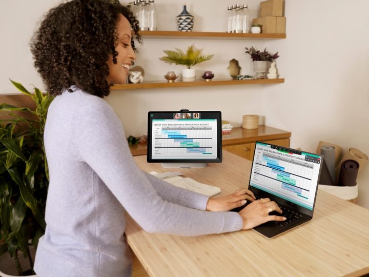 A woman is standing at a table and using a laptop with a Meta Portal display next to it