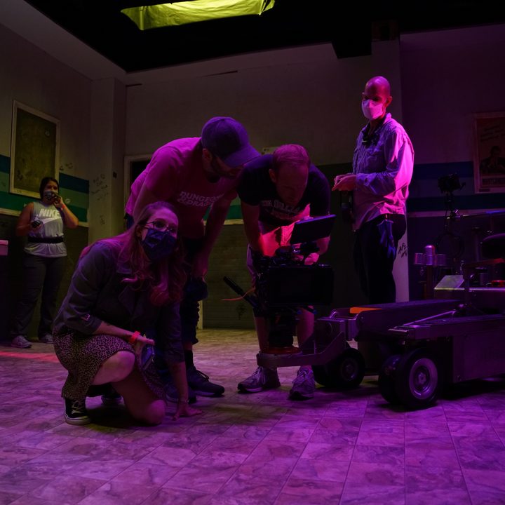 Director Rebekah McKendry kneels besides her team in a behind the scenes look at Glorious.