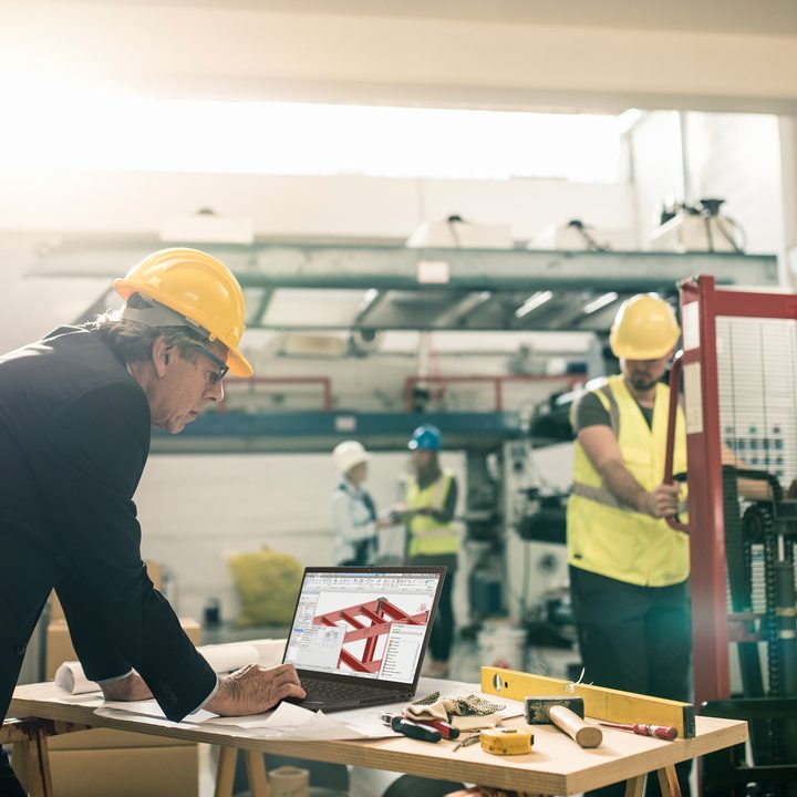 Engineer, wearing a hard hat, works on the Lenovo ThinkPad P14s as another engineer works in the background.