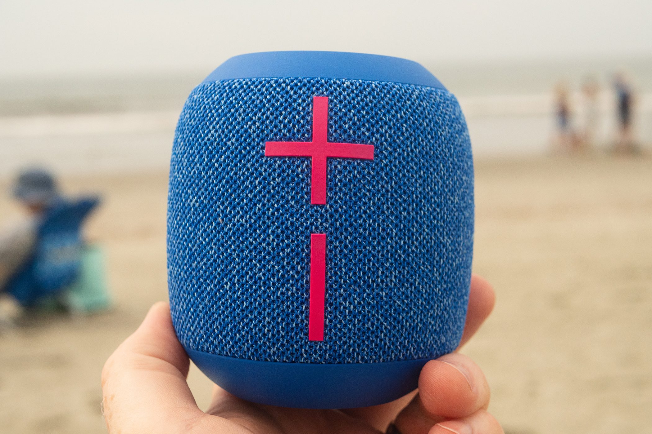A hand is holding the Wonderboom 3 speaker in front of a beach background.