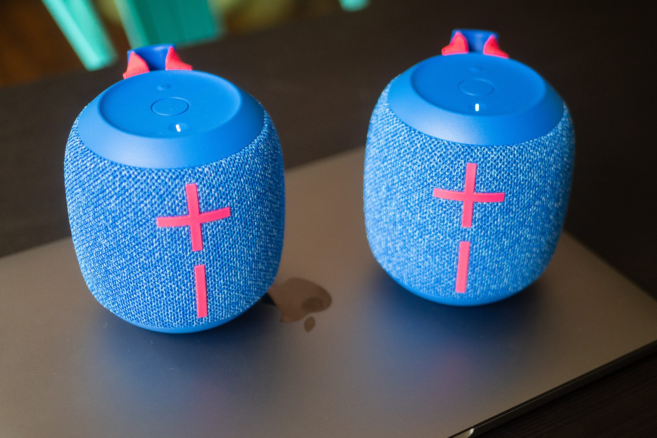 Two Wonderboom 3 speakers are sitting on top of a closed MacBook Pro on a black table.