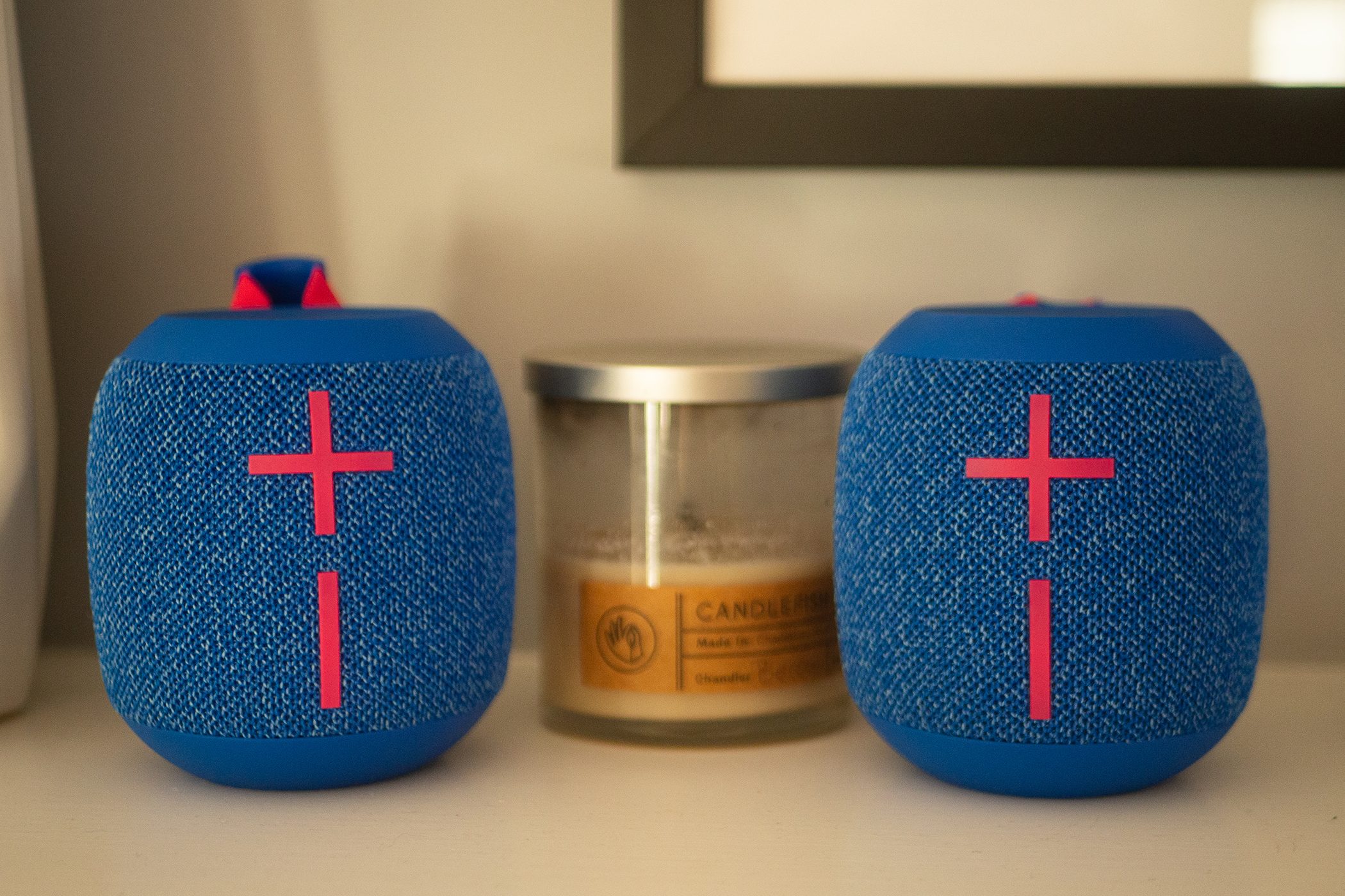Two Wonderboom 3 speakers are sitting on a white mantle with a scented candle in between them.