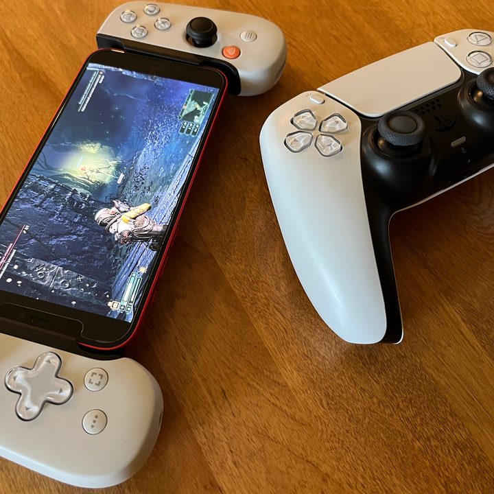 A DualSense controller sitting on a table next to a DualSense Backbone displaying the PS5 exclusive game Returnal on its screen.
