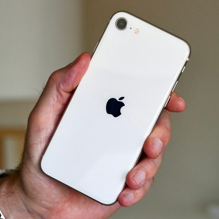 The Apple iPhone SE (2022) being held in a mans hand.