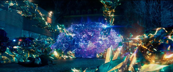 A bluish-magenta dome of crystalline hard light sits in the middle of golden shards of crystal in a parking lot.
