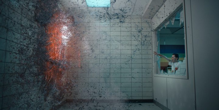 Eleven points her hand at a portal forming in the wall in front of her in a scene from Stranger Things season 4.