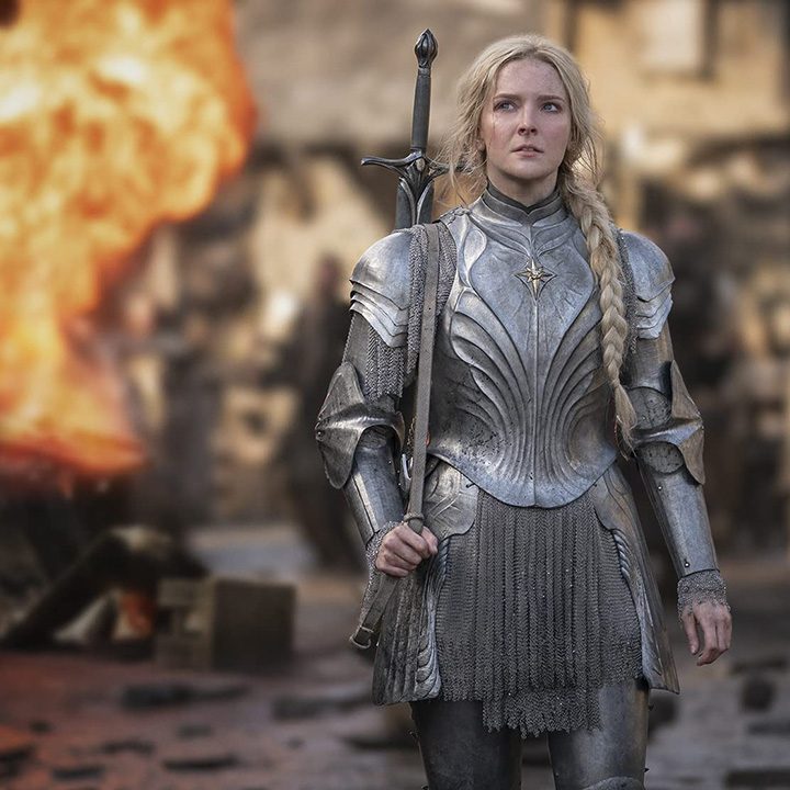 A woman walking in uniform, fire behind here in a scene from Lord of the Rings: The Rings of Power.