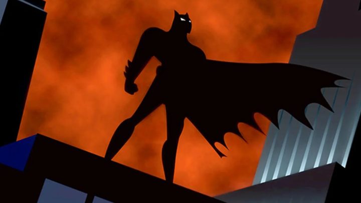 The silhouette of Batman as he stands atop a building in Gotham.