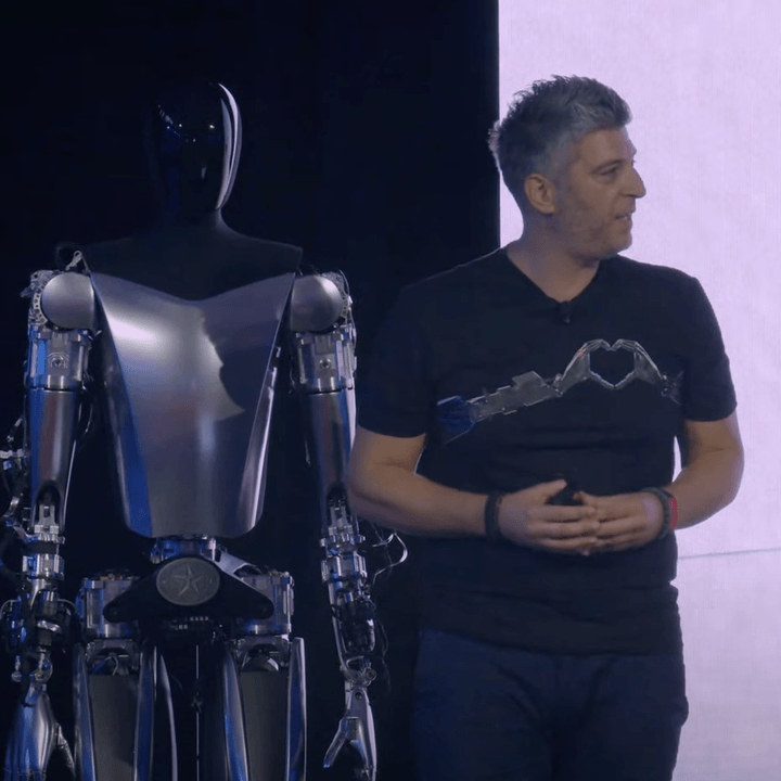 A Tesla employee standing in front of the Optimus robot.