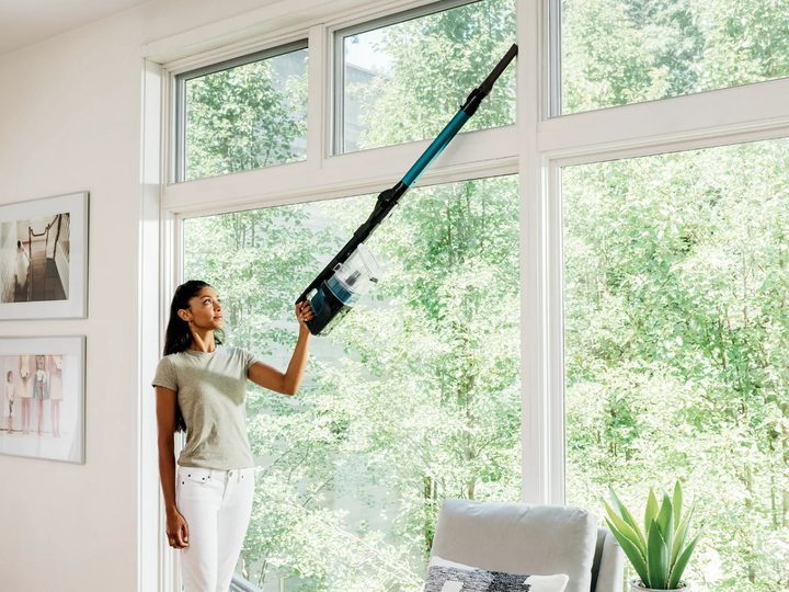 A woman using the Shark Pet Pro cordless stick vacuum to clean the windows.