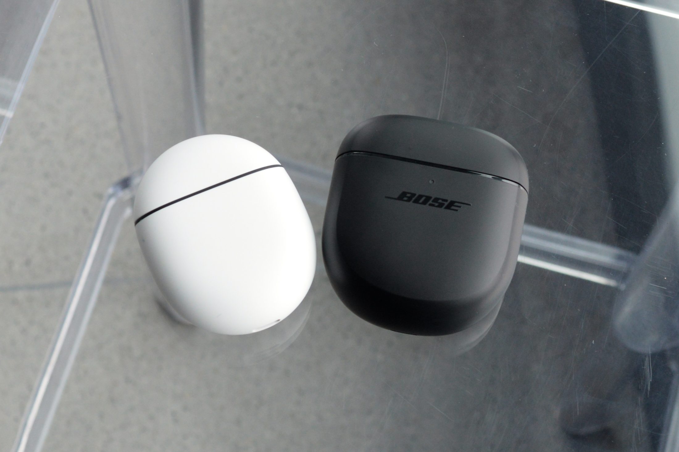 Bose QuietComfort Earbuds II charging case seen next to a Google Pixel Buds Pro charging case for scale.