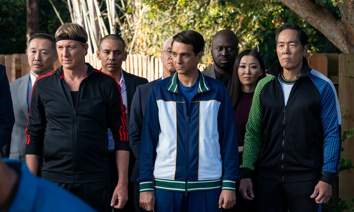 William Zabka, Ralph Macchio, and Yuji Okumoto stand in track suits in a scene from Cobr Kai season 5.