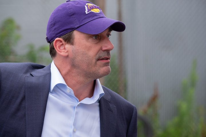 Jon Hamm stares off to the right while wearing a Los Angeles Lakers hat in a scene from Confess, Fletch.