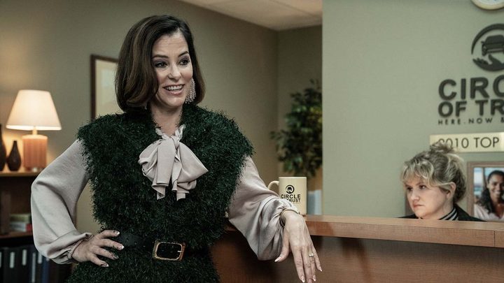 Blair leaning against the reception desk, Gina sitting down in a scene from Tales of the Walking Dead.