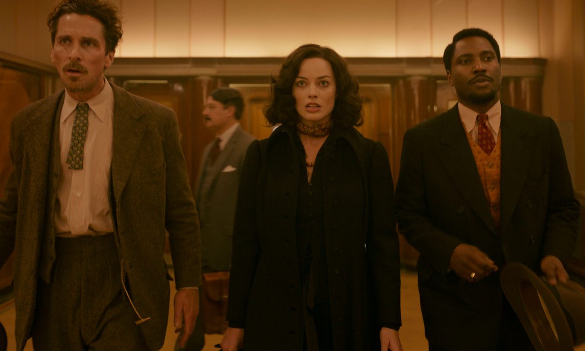 Christian Bale, Margot Robbie, and John David Washington walk through a lobby together in Amsterdam.
