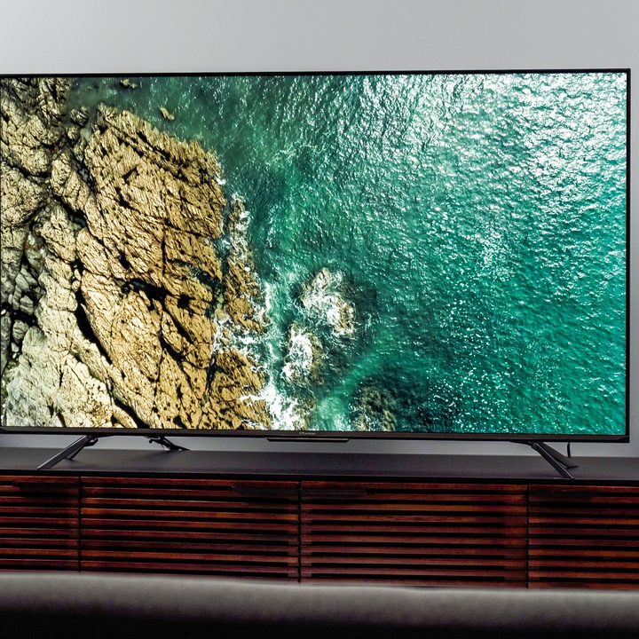 The Hisense U7H displaying a picture of an emerald green ocean crashing against a rocky cliff face.