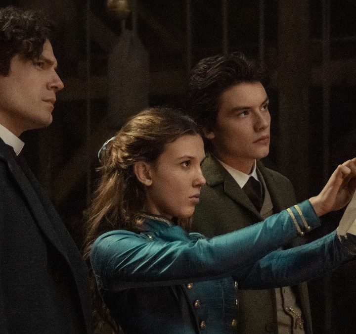 Millie Bobby Brown, Henry Cavill, and Louis Partridge stare at a piece of paper in a scene from Enola Holmes 2.