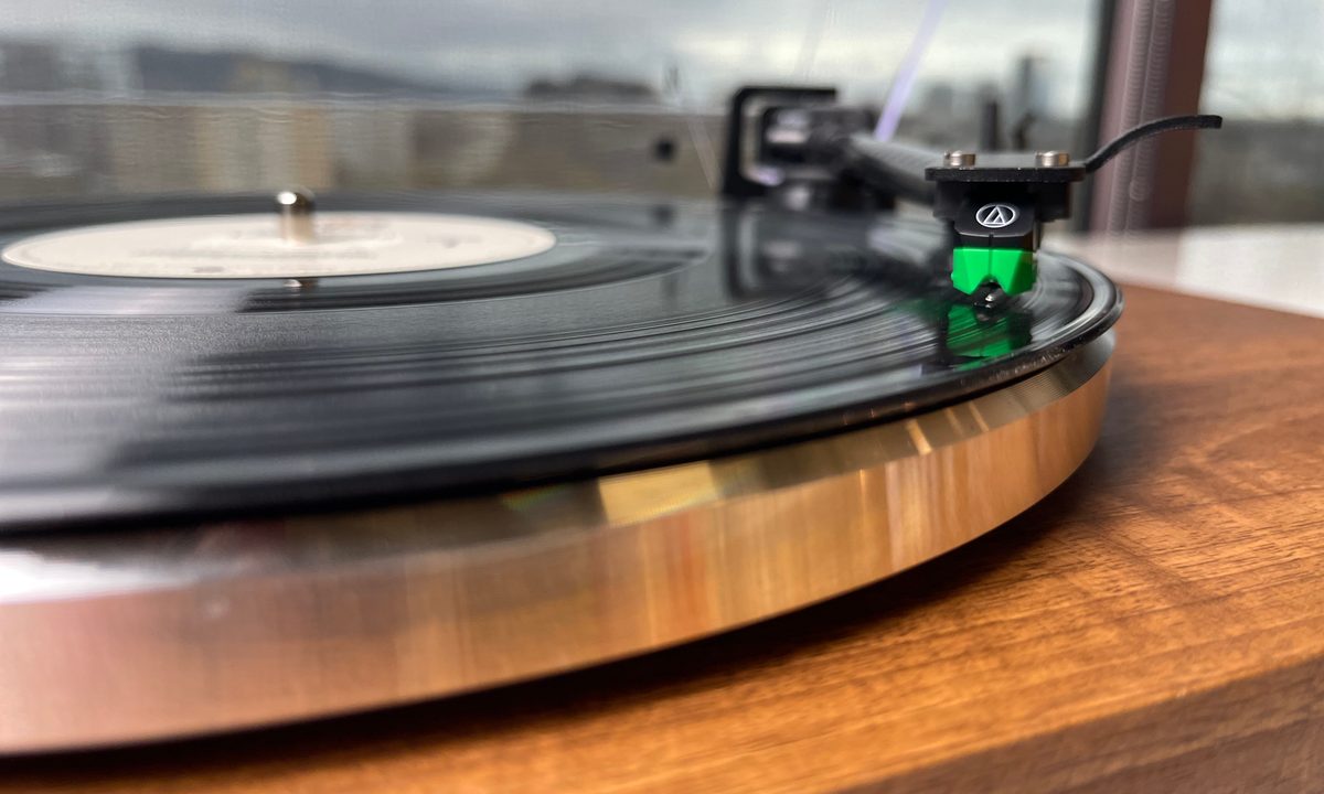 Picture of a green Audio-Technica cartridge settled into the groove of a record on the monolith turntable.