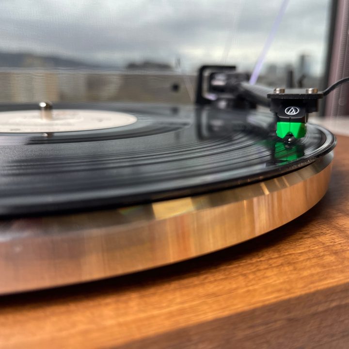 Picture of a green Audio-Technica cartridge settled into the groove of a record on the monolith turntable.