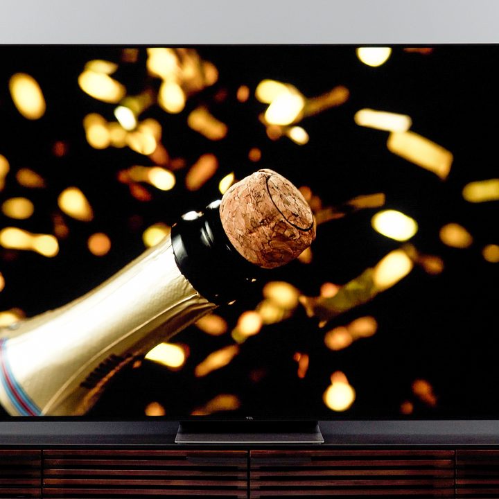A closeup of a cork and neck of a champagne bottle with gold lights in the background on a TCL 6-Series (R655) TV.