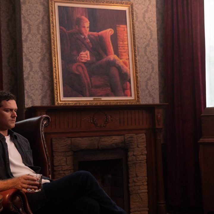 Finn Jones sits down with a glass in hand in a scene from The Visitor.