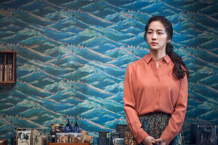 Tang Wei stands in front of intricate wallpaper in Park Chan-wook's Decision to Leave.