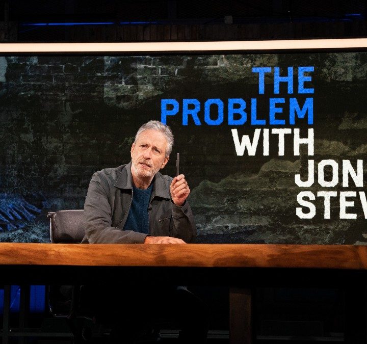 Jon Stewart sits down and points his pen in a scene from The Problem with Jon Stewart.