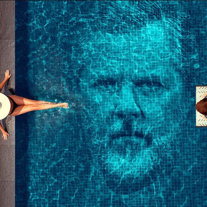 A man and a woman sit by a pool with an image of a Jerry Falwell Jr.'s face in the water.