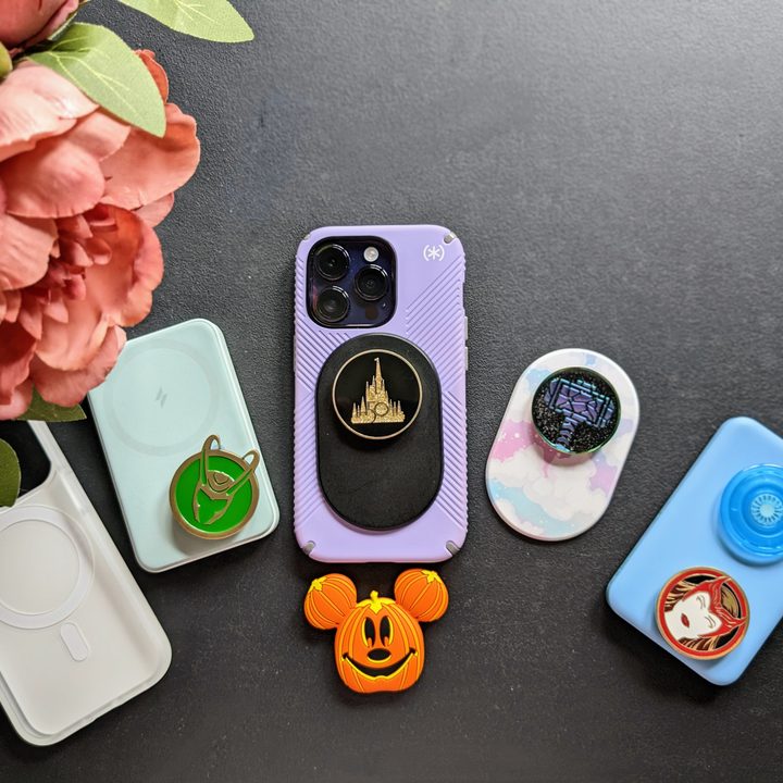 iPhone 14 Pro with Speck MagSafe Presidio Grip case on, with a black PopSocket MagSafe with Walt Disney World 50th Celebration PopSocket, along with a collection of MagSafe battery packs and PopTops.