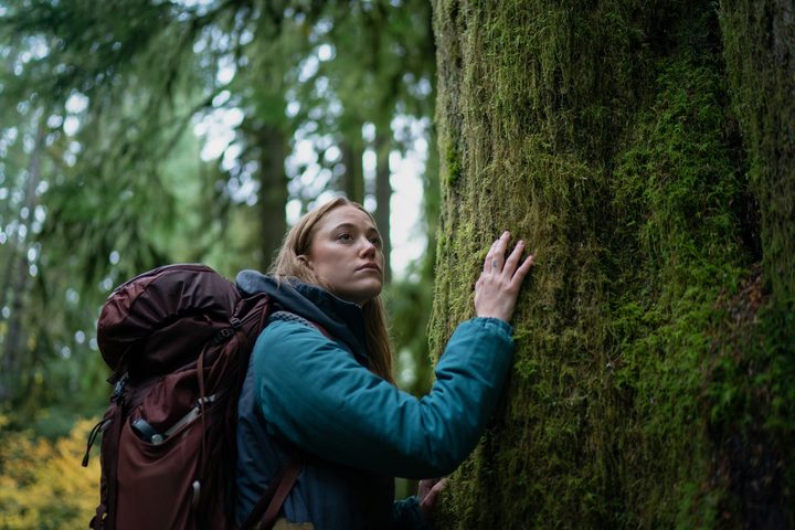Maika Monroe touchs a tree in th forest in a scene from Significant Other.