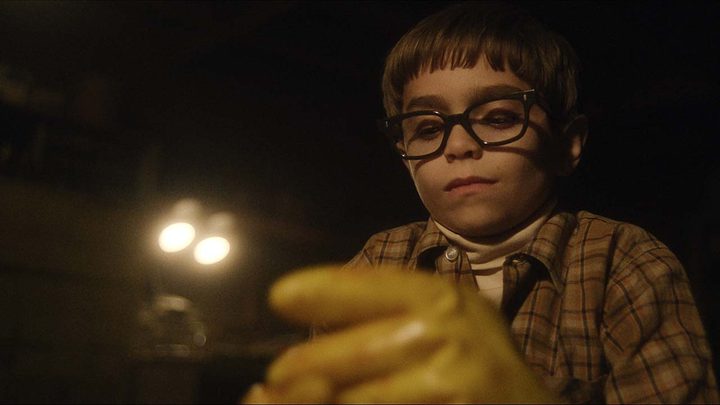 A young Jeffrey Dahmer with gloves on in a scene from Monster: The Jeffrey Dahmer Story.