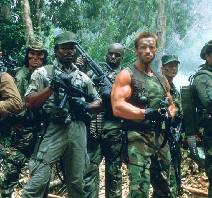 The cast of Predator poses with their guns in the jungle.