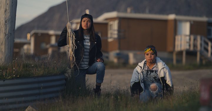 Two girls, one holding a rifle, crouch in a field in a scene from Slash/Back.