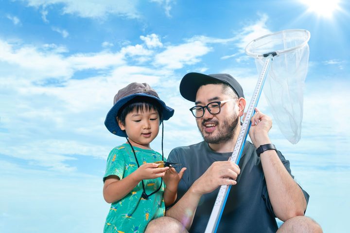 A man holds a gboard with a net at the end while a young boy stands next to him