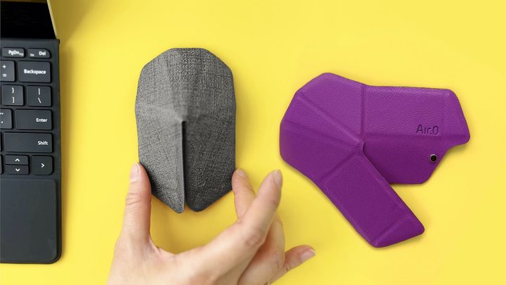 Two Air.0 mice on a desk next to a computer, with one being folded up for use and one folded down flat.