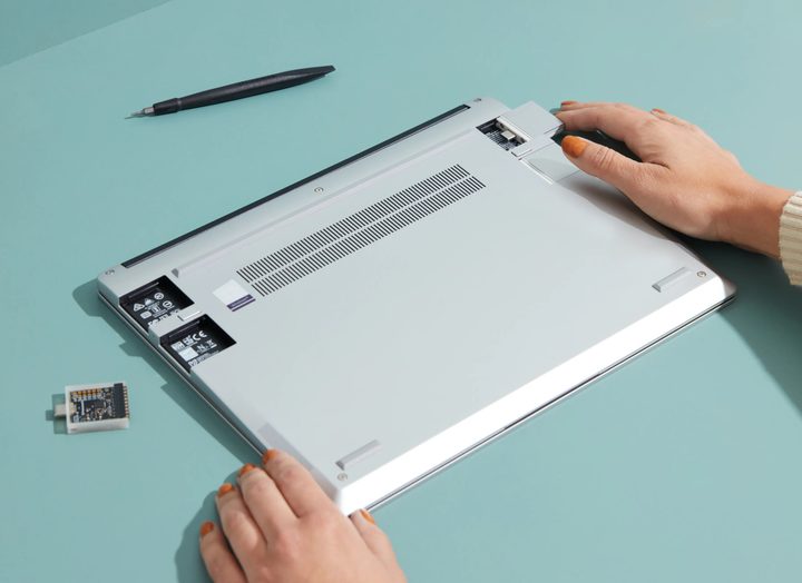 A Framework laptop upside down with two hands holding it and the USB ports unscrewed