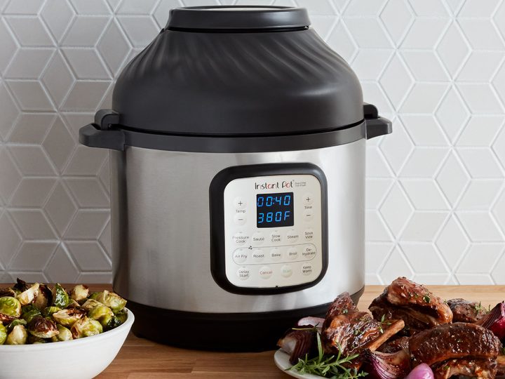 Instant Pot 6-quart Crisp Pressure Cooker Air Fryer on a counter with cooked meat and veg.