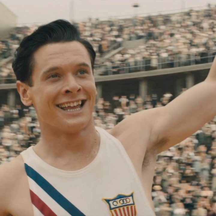Jack O'Connell smiles and raises his arm in a scene from Unbreakable.