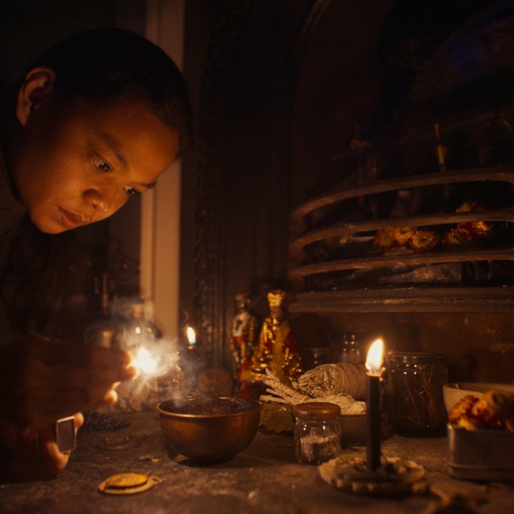 A woman lights a candle in a scene from Nocebo.