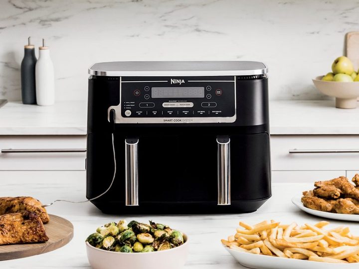 Ninja Foodi 6-in-1 10-quart XL 2-Basket Air Fryer on a white kitchen counter with a variety of air fried foods.