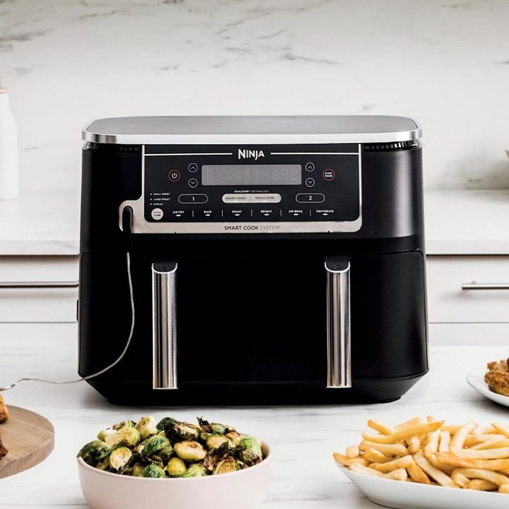 Ninja Foodi 6-in-1 10-quart XL 2-Basket Air Fryer on a white kitchen counter with a variety of air-fried foods.