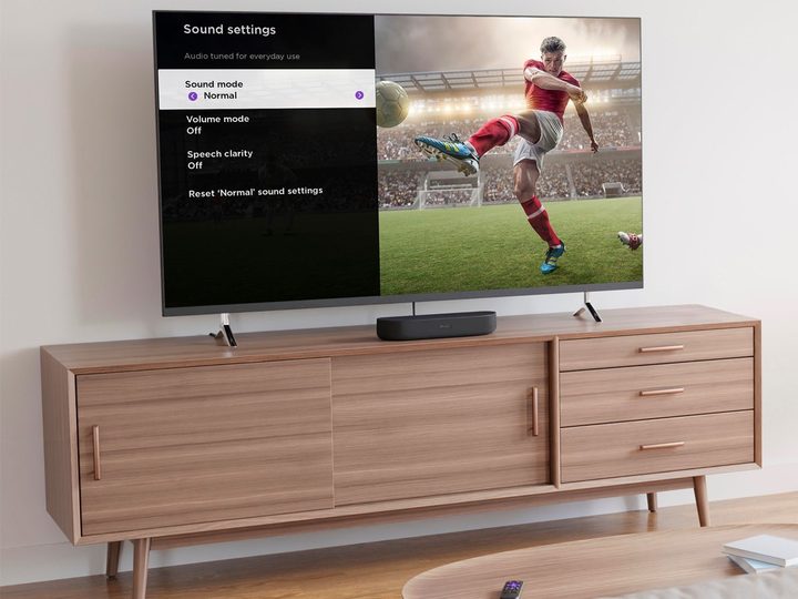 A Roku Streambar on a cabinet with a TV.