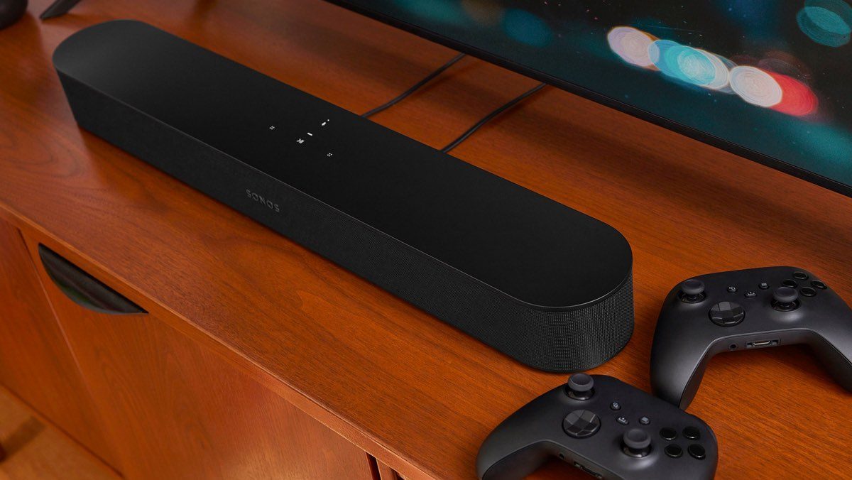 The Sonos Beam 2 soundbar on a media cabinet with a couple of video game controllers.