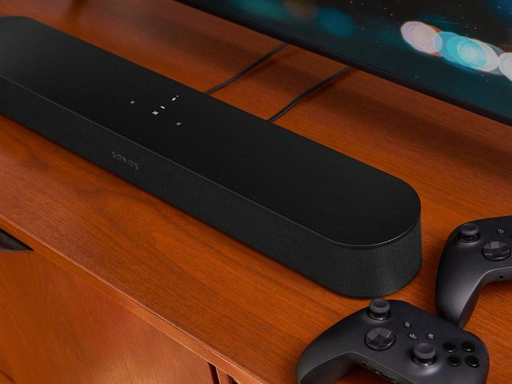 The Sonos Beam 2 soundbar on a media cabinet with a couple of video game controllers.