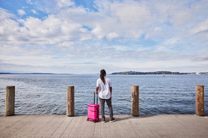 A woman standing at the edge of a dock with the bright pink T-Mobile Un-carrier On suitcase.