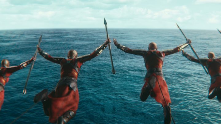 The women of the Dora Milaje dive over the side of a boat, spears in hand, in a scene from Black Panther: Wakanda Forever.