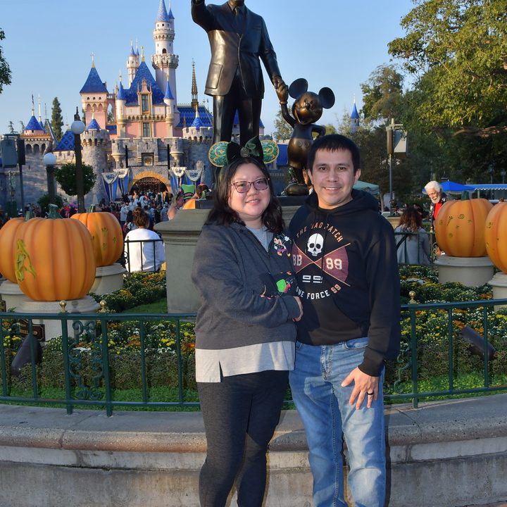 Christine and husband pose in front of the Walt Disney and Mickey Partner Statue at Disneyland.