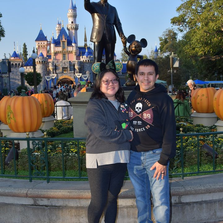 Christine and husband pose at Disneyland's Walt and Mickey partner statue.